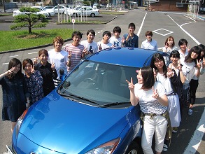 水俣自動車学校の合宿教習生が教習車の横で記念撮影した写真